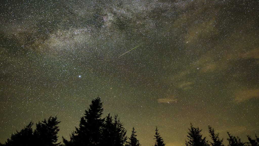 Céu estrelado com a Via Láctea e o rasto fino de um meteoro