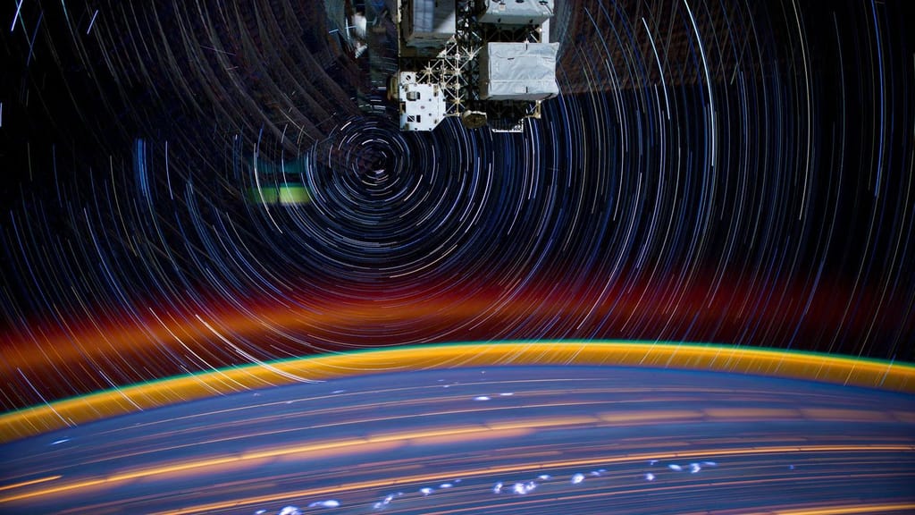 Fotografia de longa exposição tirada da Estação Espacial Internacional, com rastos de estrelas em arco sobre o limbo da Terra e a fina camada azul da atmosfera
